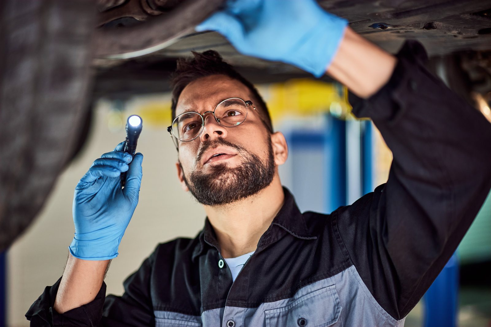Mechanic inspecting the underside of a vehicle with a flashlight