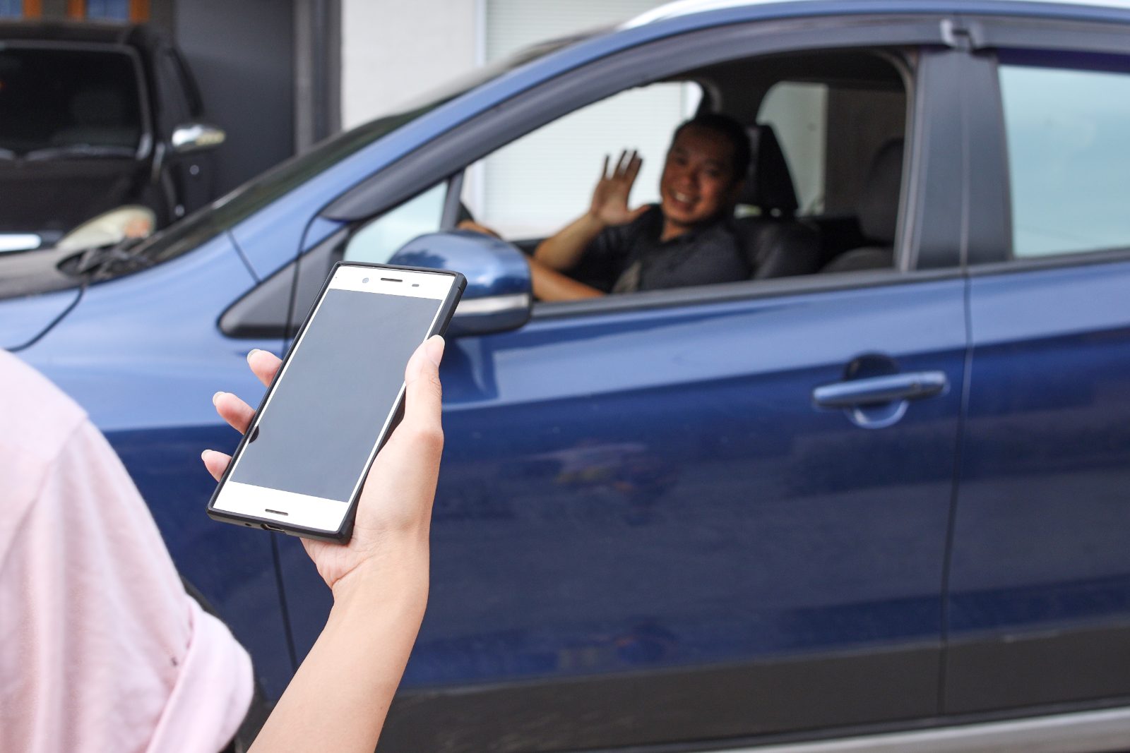 Rideshare passenger holding a phone as the driver waves from a car